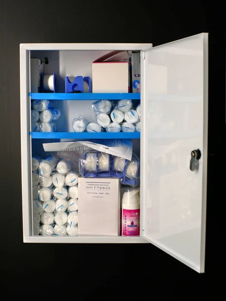 stock image  First aid cabinet mounted on a black wall, filled with bandage, antiseptic spray... Door is open. 