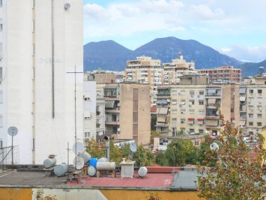 Tiran 'daki bir binanın çatısına yerleştirilmiş sarnıçlar, su tankları ve uydu antenleri. Arka planda, şehir dağlarla çevrili..