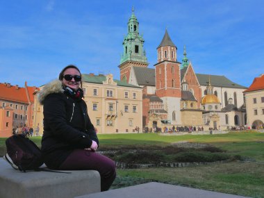 Wawel castle under a blue sky. A woman is sitting in front of it, on a concrete seat.