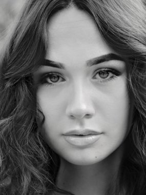 Close black and white portrait of a young brunette woman face, with brown eyes, long hair.