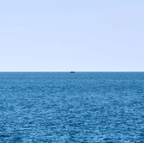 stock image Minimalist composition including the Mediterranean sea and a cloudless sky, with a distant boat in the center.