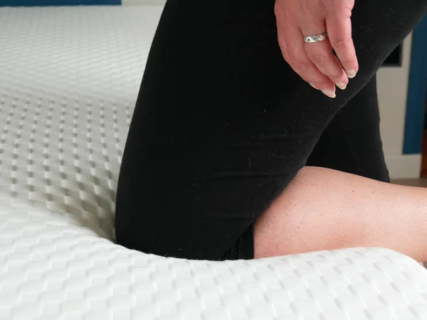 Woman testing the softness of a new mattress. Her knee sinks slightly