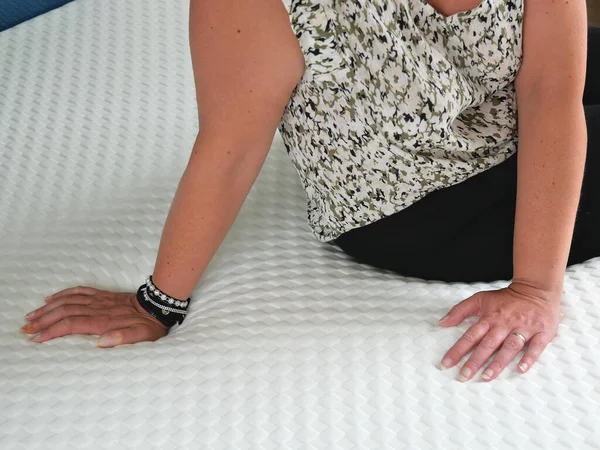 Woman testing the softness of a new mattress. Her hands sinks slightly