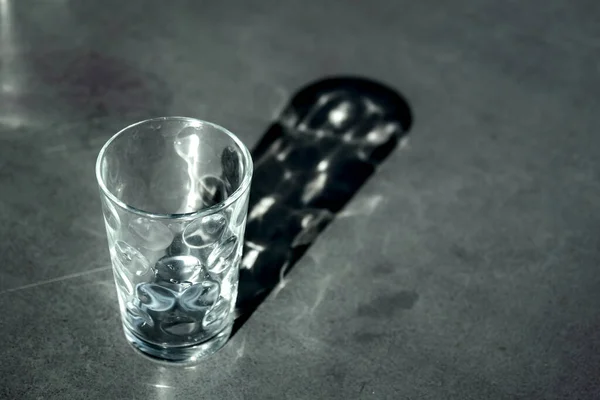Empty glass and its shadow projected onto a grey table.