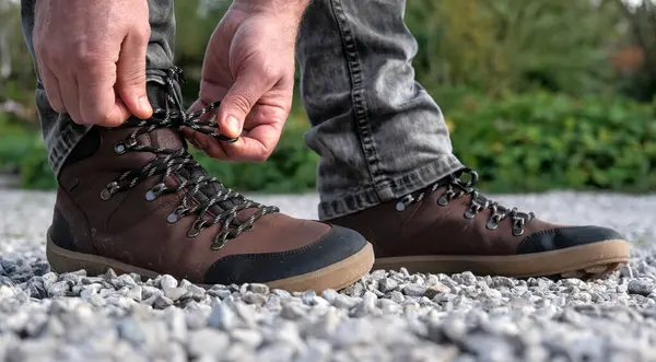 Close-up of hiking boots, walking on gravel. Men's hands retie the laces.