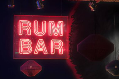 Sıcak, karanlık bir atmosferde, üzerinde RUM BAR yazısıyla aydınlatılmış kırmızı tabela.. 