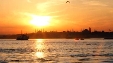 İstanbul, Sultanahmet camilerinin siluetleri, Aziz Sophia (Ayasofya) ve muhteşem bir günbatımı ile özetlenen Boğaz 'da yelken açan bir tekne..