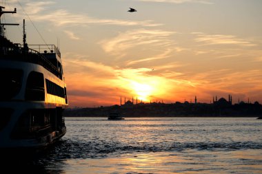 Sultanahmet ilçesinin silueti ve camileri renkli bir günbatımında. Boğaz 'da bir tekne hareket ediyor..