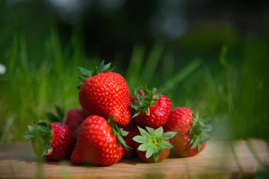 Çimlerin üzerindeki ahşap bir tahtanın üzerindeki büyük çilek yığını.