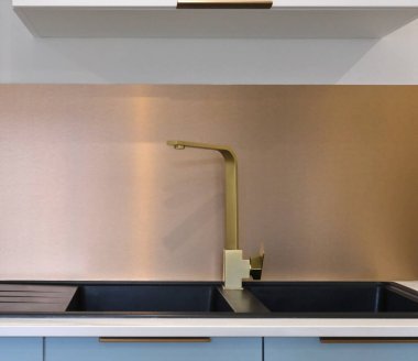 Altın-bronz musluk, siyah granit lavabonun üzerinde, bronz metalize bir büfenin önünde..