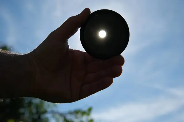 stock image Hand holding an ND filter in front of the sun. The filter attenuates the amount of light passing through.