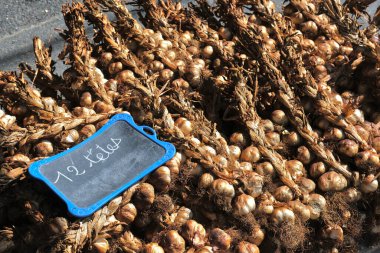 Braids of garlic heads, stacked on a pallet. A slate indicates twelve heads. clipart