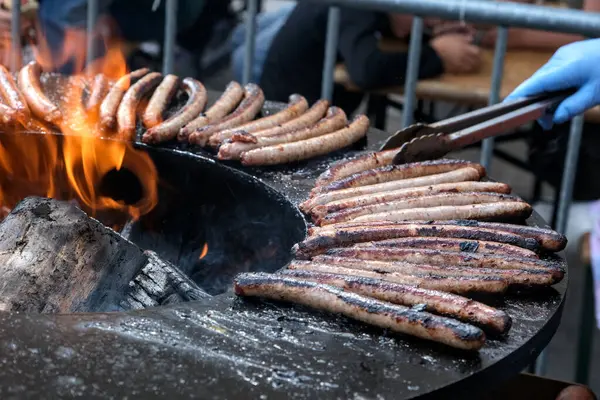 Büyük dairesel bir barbeküde pişen bir dizi sosis ve merkezi bir ateş püskürtüsü..