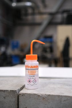 Kırmızı gagalı etanol şişesi. Şişe gövdesinde farklı çeviriler, kimyasal piktogramlar ve formüller gösterilir..