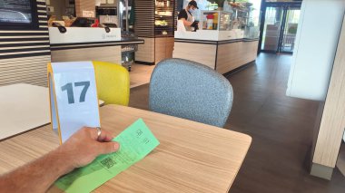 Petite Foret, Fransa - 08 31 2024: McDonald 's restoranındaki bir masada elinde sipariş bileti olan bir adamın eli. Restoran boş..