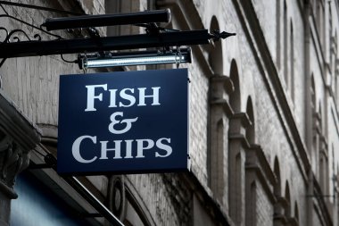 Duvarda asılı mavi bir tabela, üzerinde beyaz harflerle Fish and Chips yazıyor..