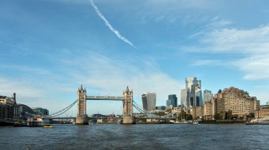 Londra 'nın Thames Nehri üzerindeki ikonik Tower Köprüsü' nün panoramik bir görüntüsü, arka planda açık mavi gökyüzünün altında modern gökdelenler var. Tarihi mimariyle şehir siluetinin mükemmel bir karışımı..