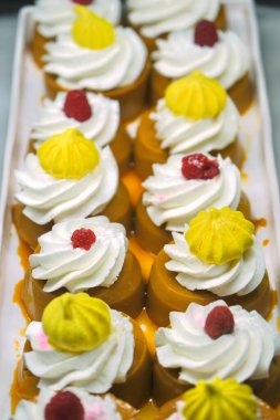 Krem şanti, ahududu ve sarı kremalı bir tepsi karamel renkli tatlı. Canlı renkler ve karışık malzemeler bunu görsel olarak çekici kılıyor..