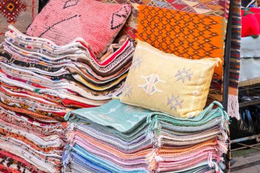  Katlanmış tekstil ve yastıkların renkli bir görüntüsü. Bir markette ya da dükkanda karmaşık desenler var. Canlı renkler ve detaylı tasarımlar onu görsel olarak çekici kılıyor..
