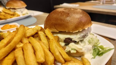 Eritilmiş Maroilles peynirli gurme burger, marul ve yumuşak brioche ekmeği, sıcak bir restoranda, beyaz bir tabakta kızarmış altın patates ile servis edilir..