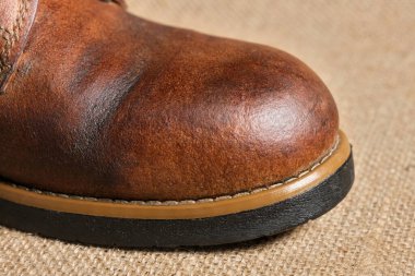 Görünür kırışıklıkları, püreleri ve sağlam dikişleri olan aşınmış kahverengi deri bir botun yakın çekimi. Kırsal arka plan engebeli, klasik estetiği güçlendirir..