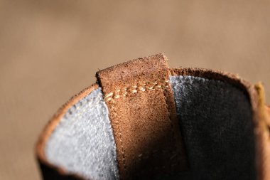 Görünür kırışıklıkları, püreleri ve sağlam dikişleri olan aşınmış kahverengi deri bir botun yakın çekimi. Kırsal arka plan engebeli, klasik estetiği güçlendirir..