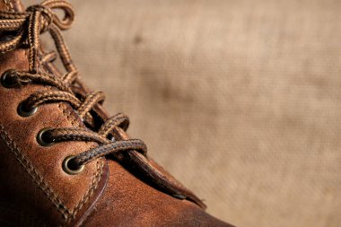 Görünür kırışıklıkları, püreleri ve sağlam dikişleri olan aşınmış kahverengi deri bir botun yakın çekimi. Kırsal arka plan engebeli, klasik estetiği güçlendirir..