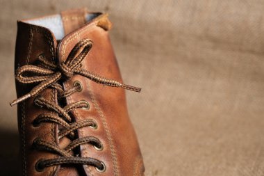 Görünür kırışıklıkları, püreleri ve sağlam dikişleri olan aşınmış kahverengi deri bir botun yakın çekimi. Kırsal arka plan engebeli, klasik estetiği güçlendirir..