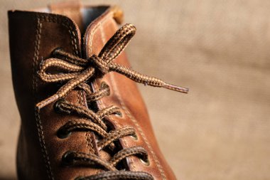 Görünür kırışıklıkları, püreleri ve sağlam dikişleri olan aşınmış kahverengi deri bir botun yakın çekimi. Kırsal arka plan engebeli, klasik estetiği güçlendirir..