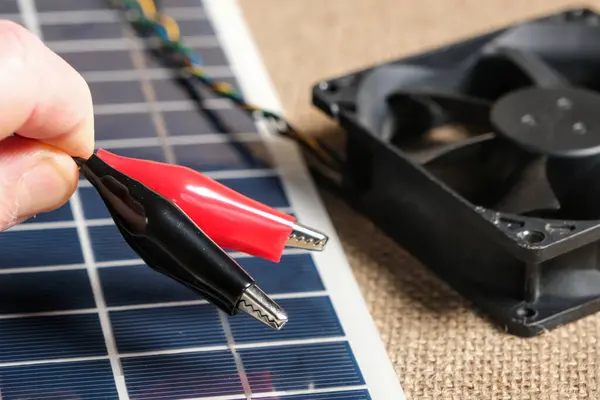 Güneş panelinin yakın çekimi, timsah klipleri ve DIY yenilenebilir enerji projesini temsil eden soğutma vantilatörü. Güneş enerjisi ve sürdürülebilir teknoloji kavramı.