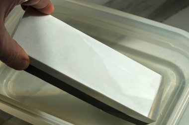 Plastik bir kabın içinde bilenmeye hazır, suya batırılmış bir bileme taşı.. 