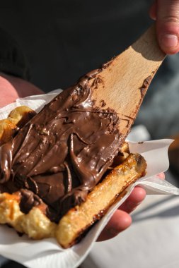 Yeni pişmiş Belçika waffle 'ı ahşap bir spatula kullanılarak yumuşak, erimiş çikolatayla kaplanarak lezzetli ve zengin bir sokak yemeği oluşturulur..