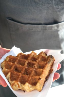 Bir el, peçeteye sarılı altın gibi, çıtır bir Belçika waffle 'ını tutuyor, tadını çıkarmaya hazır..