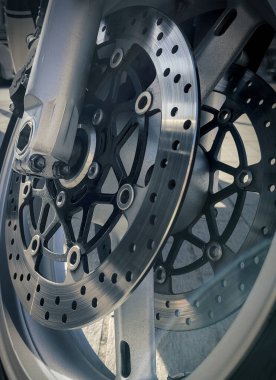 Motosiklet ön fren sistemine yakın çekim. Detaylı metal dokuları, kalibreleri ve doğal gün ışığı altında delinmiş pervaneleri gösteriyor..