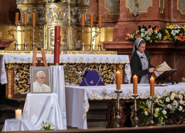 Poznan, Polonya - 04 22 2025: Bir rahibe kilisede okuyor. Solda, merhum Papa Franois 'in çerçeveli bir resmi sergilenmektedir. Sunakta mumlar, çiçekler ve dini eşyalar var. Sadakati simgeliyor.
