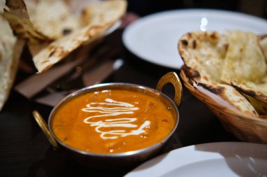 Portakal kırmızısı soslu, beyaz çiselemeyle süslenmiş, siyah bir masada naan ekmeğiyle servis edilen bir kase kremalı tikka masala tavuğu..