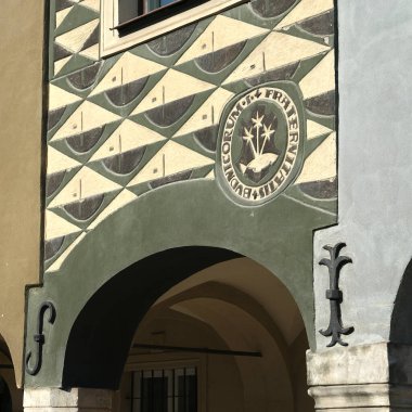 Pozna Rynek 'teki tarihi bir tüccar evinin dekoratif cephesinde geometrik desenler, Latince yazılar ve güneş ışığı altında dini amblemler yer alıyor..