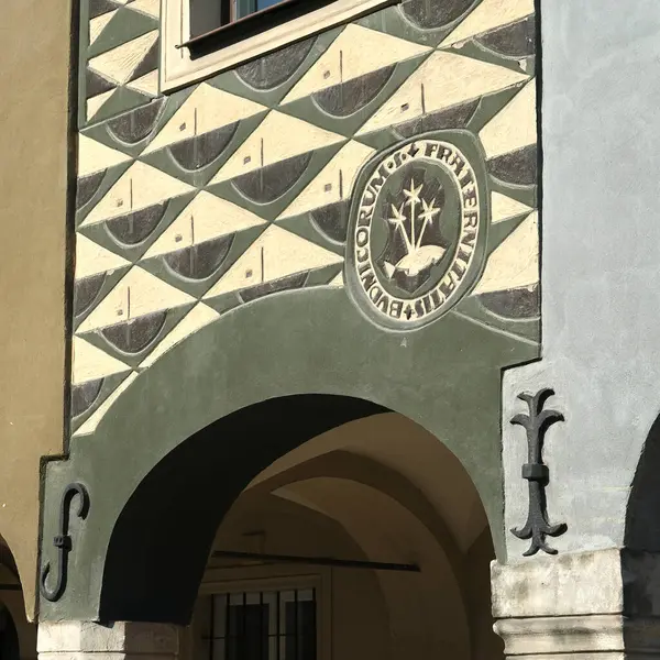 Pozna Rynek 'teki tarihi bir tüccar evinin dekoratif cephesinde geometrik desenler, Latince yazılar ve güneş ışığı altında dini amblemler yer alıyor..