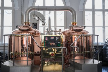 Poznan, Polonya - 04 22 2025: Bira fabrikasında bira demleyen modern bakır bira imalathanesi, paslanmaz çelik borular, kontrol paneli ve doğal ışık üreten ekipmanlar.