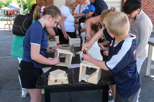 Bouchain, Fransa - 05 10 2025: Çocuklar ve yetişkinler açık hava halk etkinliğinde birlikte kuş evleri inşa ederek ahşap işçiliği faaliyetlerine katılıyorlar.