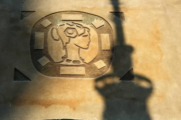 Poznan 'da güneşli bir ticaret evinin duvarındaki kadın profilinin taş tasfiyesi, bir sokak lambasının gölgesi derinlik ve görsel entrika ekliyor..