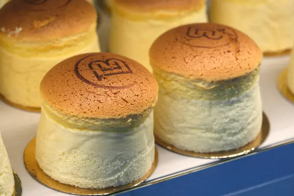 Altın kaplamalı pofuduk Japon peynirli kekleri yakın plan, bir pastane vitrininde sergileniyor, satışa hazır..