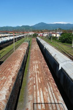 Batumi, Gürcistan - 05: 20 2025: Paslı ve yıpranmış yük vagonları açık mavi gökyüzünün altındaki bir sanayi deposunda demiryolu raylarına dizildi.