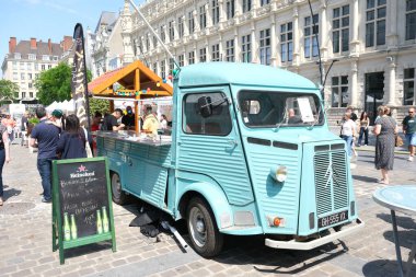 Valenciennes, Fransa - 05: 31 31: 2025: Turkuaz vintage gıda kamyonu, neşeli bir Avrupa pazarında güneşli gökyüzü altında, insanların toplandığı yemekler sunuyor..