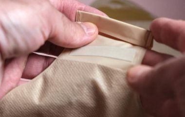 Eller bir ostomi torbasının alt boşaltma bölümünü tutuyor. Hijyenik boşaltımda ve torbanın bakımında kullanılan güvenli kapanışı gösteriyor..