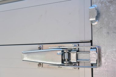 Sahil evinin yanındaki çakıl yolu üzerinde rampası olan alüminyum karavan ve güneşli, bulutlu gökyüzünün altında canlı bir bahçe. Karavan duvarı kilitleme sistemi.