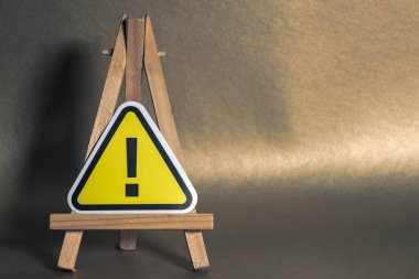 Ahşap sehpada ünlem işareti olan sarı uyarı işareti, kahverengi bir arka plana ayarlanmış, ihtiyatı ve uyarıyı simgeliyor..