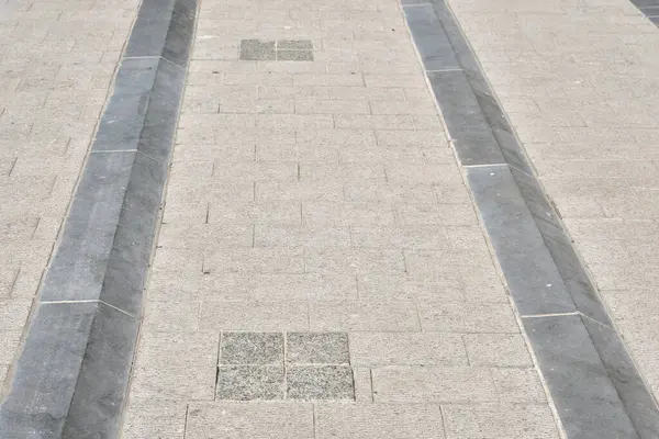 Doğal taş kaldırımlı mavi bir kaldırıma yakın çekim, şehir dokusunu, geometriyi ve açık hava ışıklarındaki nötr tonları gösterir..