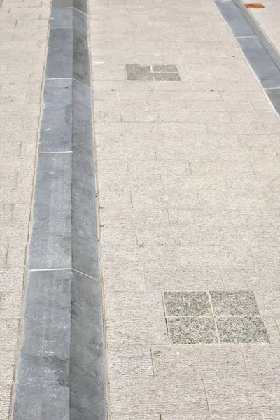 Doğal taş kaldırımlı mavi bir kaldırıma yakın çekim, şehir dokusunu, geometriyi ve açık hava ışıklarındaki nötr tonları gösterir..