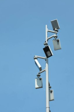 Geniş alan güvenlik gözlemi için tasarlanmış açık mavi gökyüzüne karşı çoklu güvenlik kameraları ve LED ışığı olan uzun bir direk..